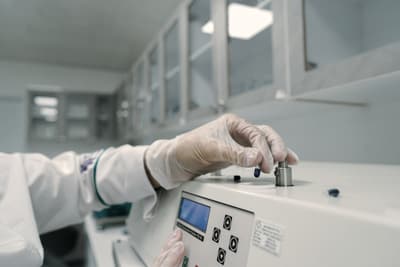 A gloved hand placing a small sample into a laboratory analyser