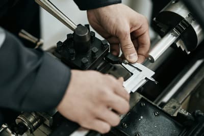 Hands measuring a machined steel rod with a vernier caliper at a lathe