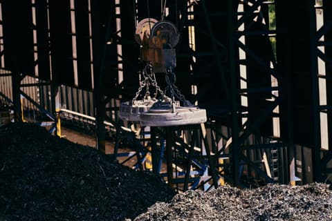 A lifting magnet over neat piles of steel scrap in a covered scrap bay